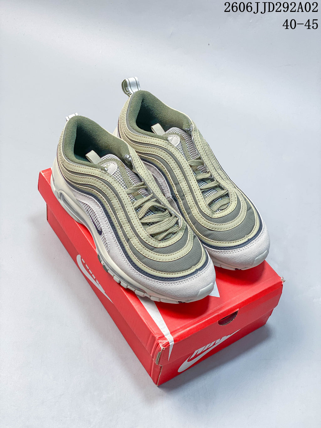 Pair of Nike Air Max 97 sneakers in muted green, gray, and white, shown on a red shoe box