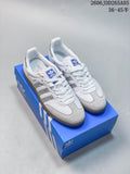 White adidas Samba OG sneakers with silver-look stripes and heel accents, shown on a blue shoe box.