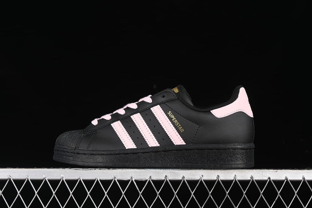 Side view of a black adidas Superstar sneaker with pink stripes, laces, and heel tab