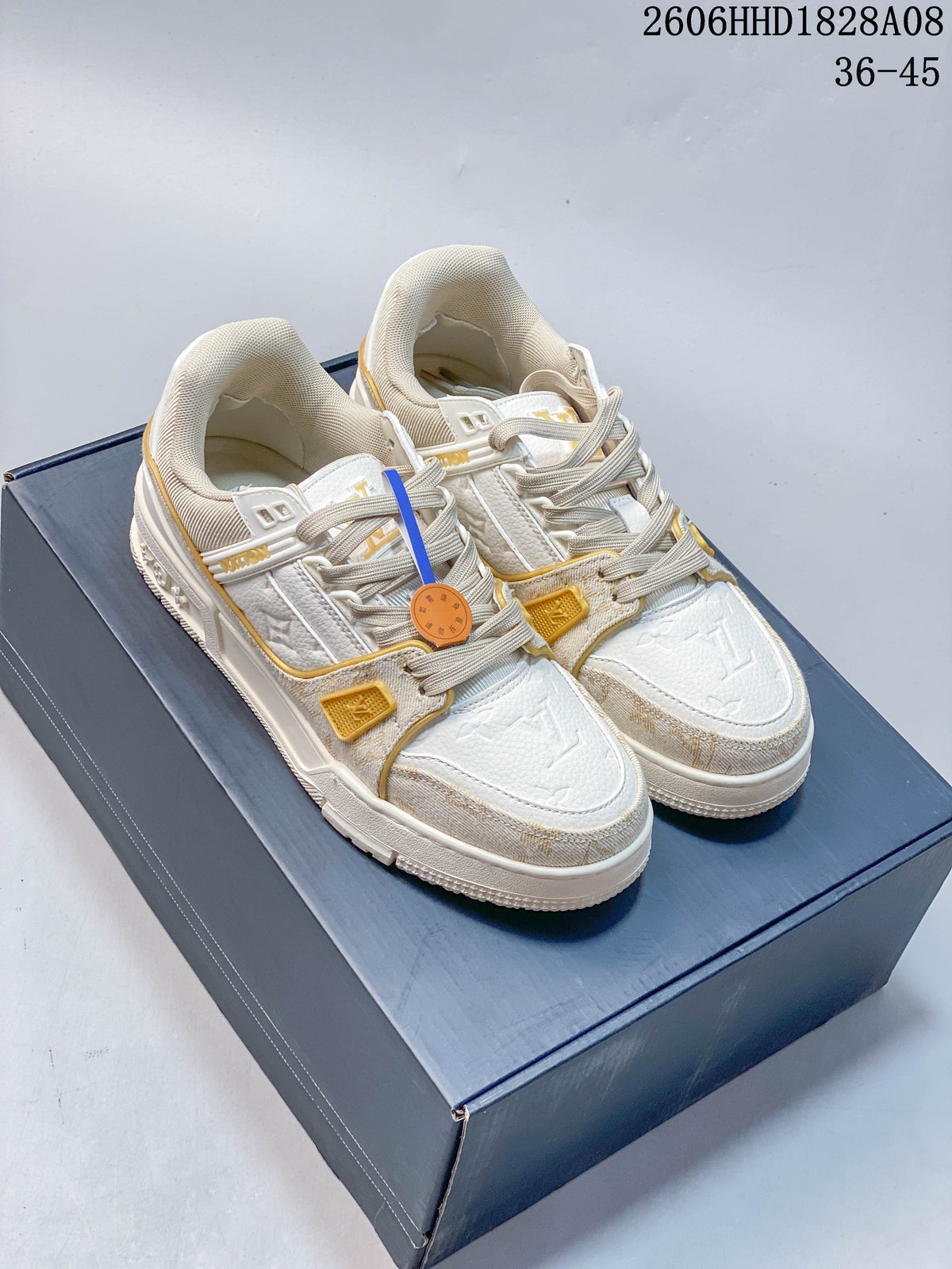 Pair of white and beige low-top sneakers with gold-tone accents, shown from above.