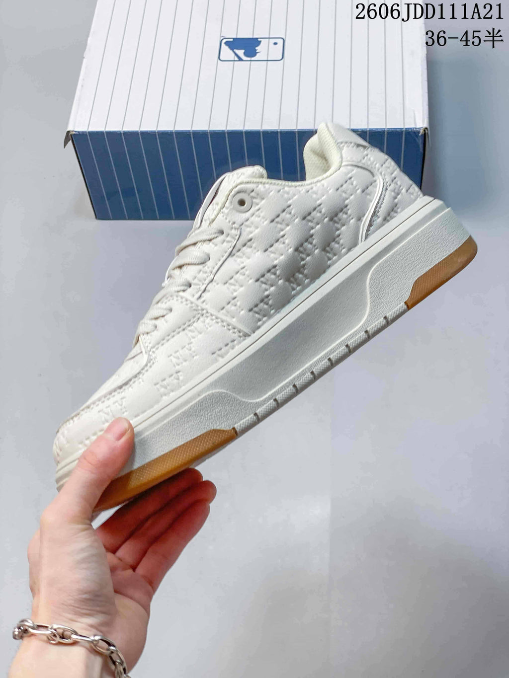 Side view of an ivory low-top sneaker with an embossed monogram pattern