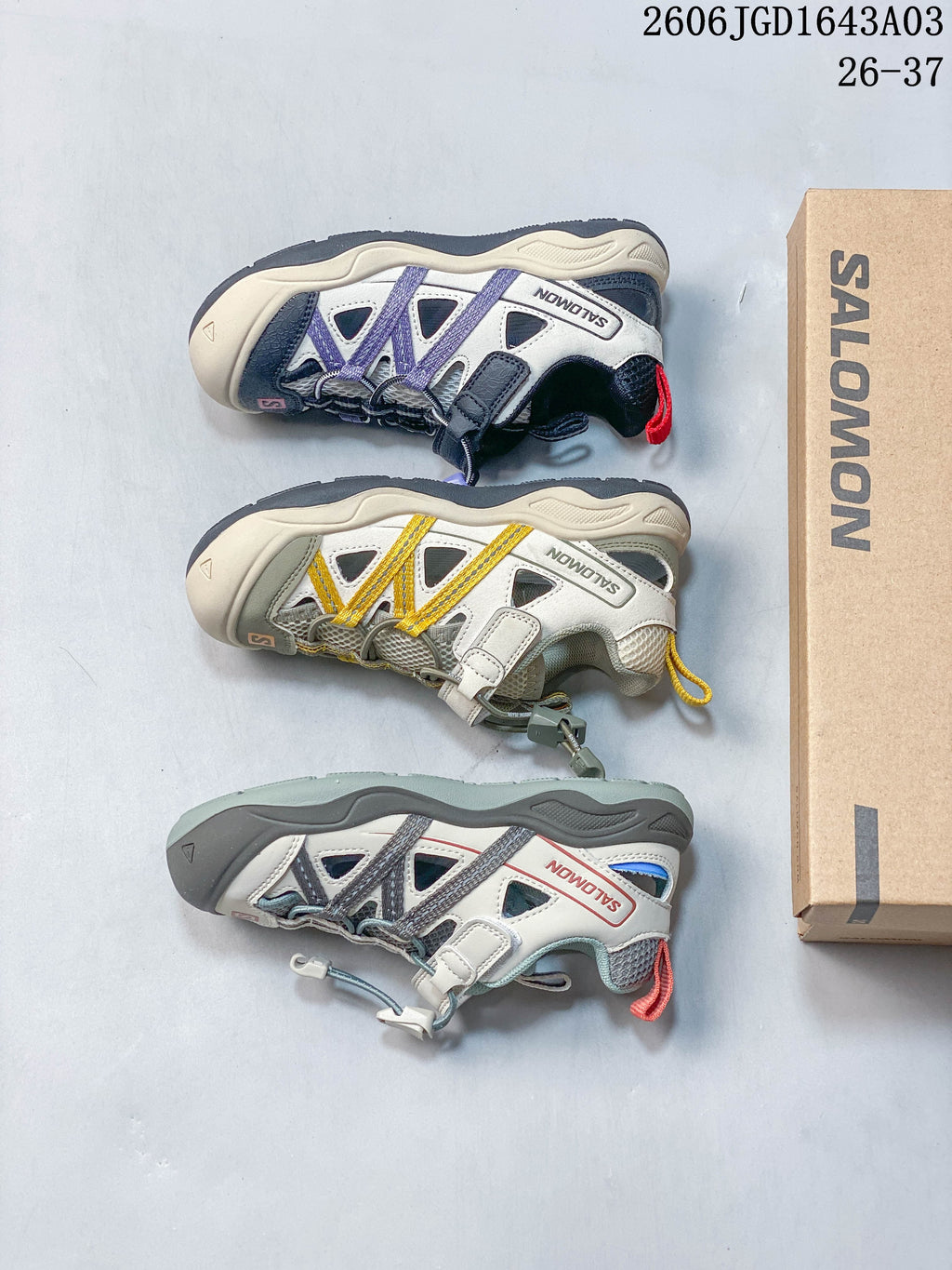 Three color combinations of kids’ Salomon sneakers arranged beside a Salomon shoe box.