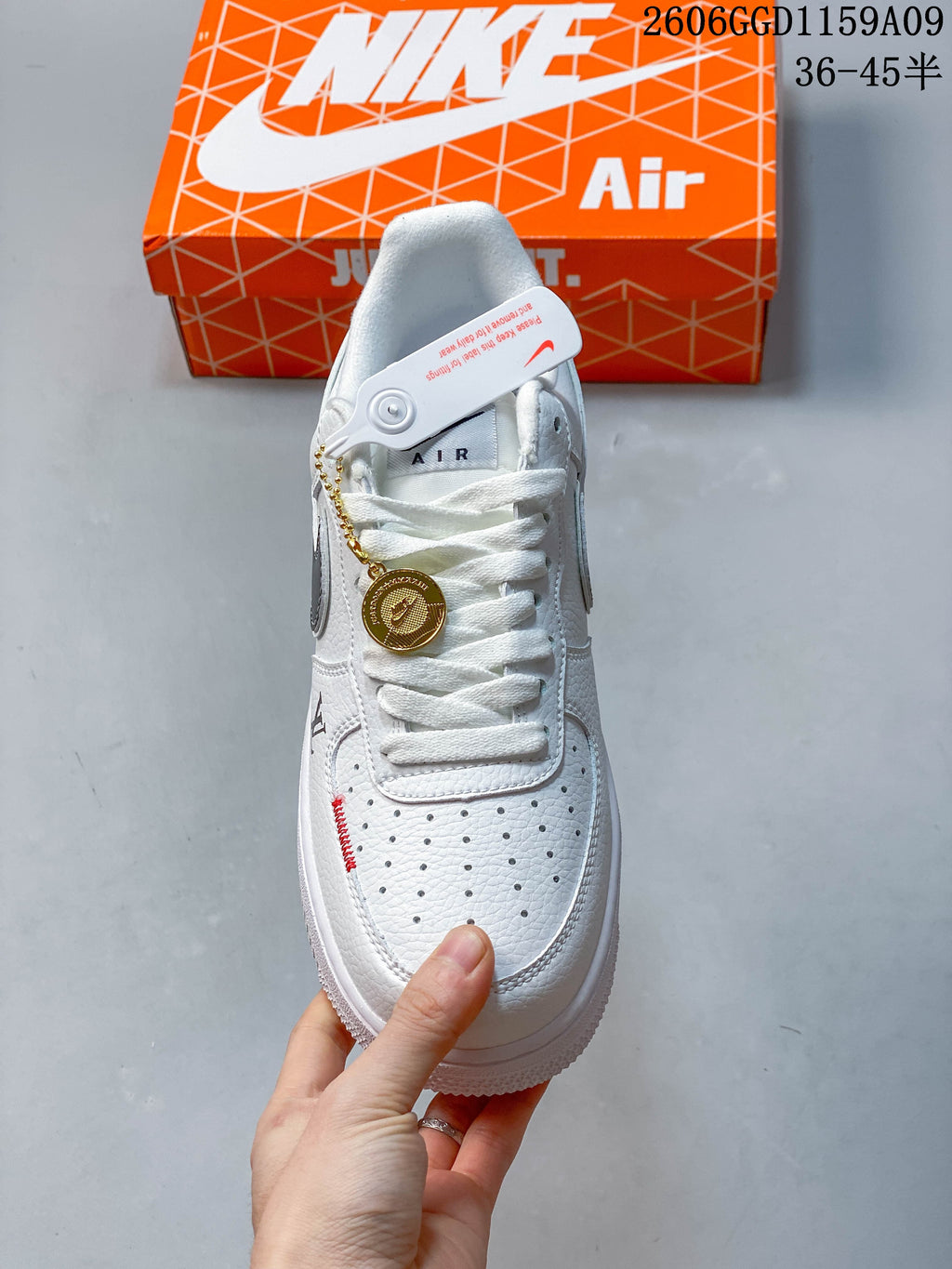 Top view of a white sneaker with laces, a perforated toe, and a gold-tone hanging charm