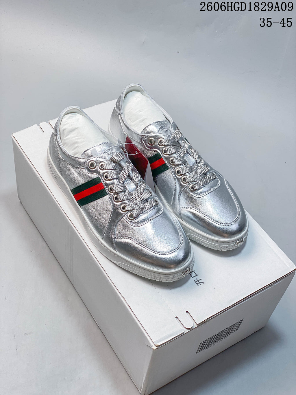 Pair of silver low-top sneakers with green-and-red side stripes on a white box.