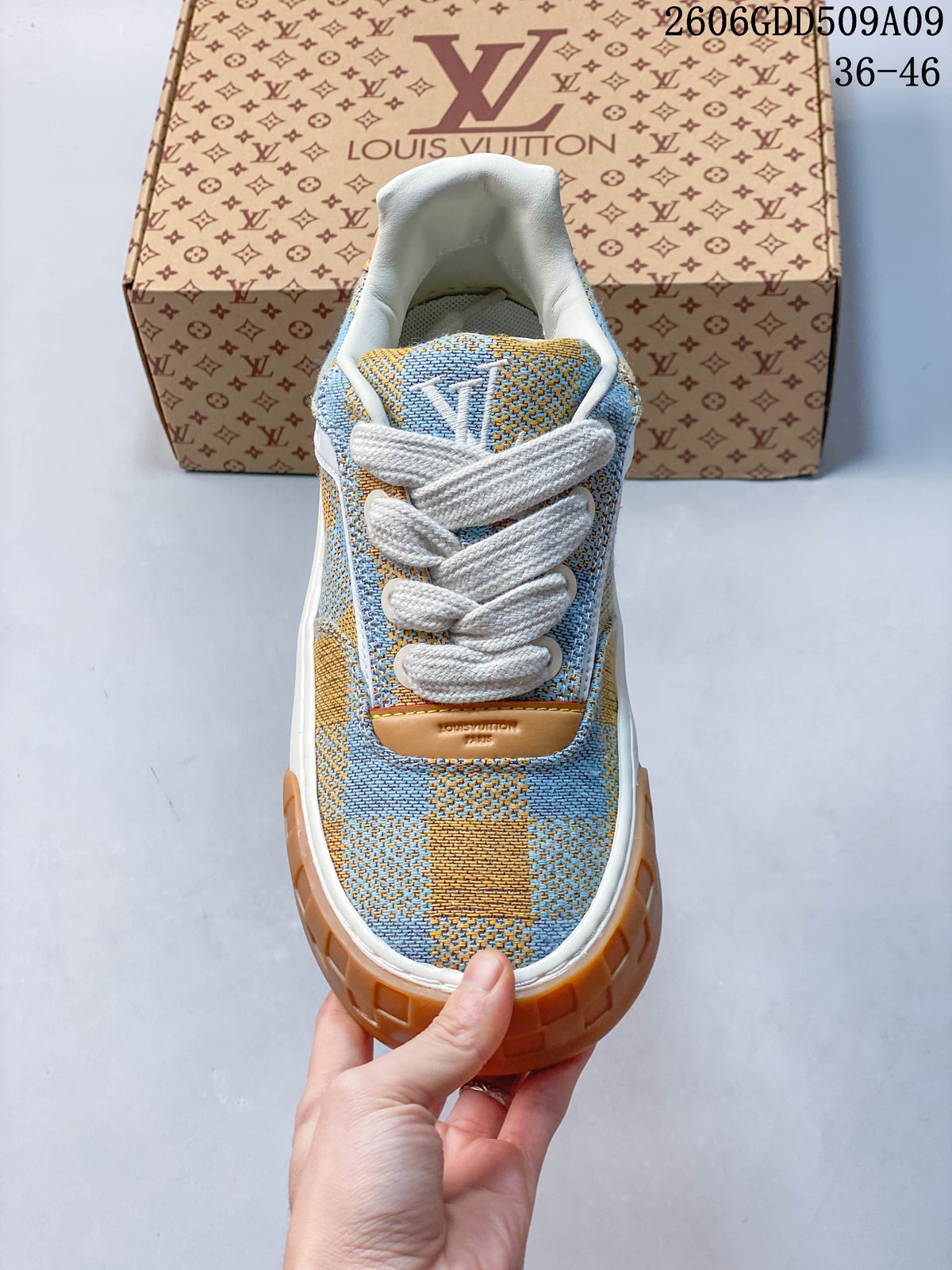 Front view of sneaker showing blue and tan check-patterned upper and white laces.