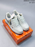 White and grey low-top sneakers with patterned side panels and a small hanging charm, shown on an orange shoe box.