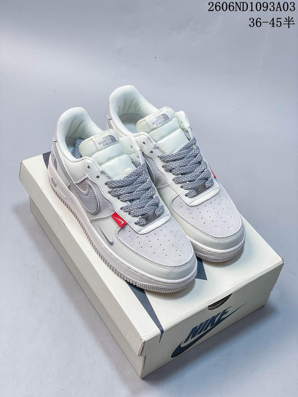 Pair of white and gray low-top sneakers with gray laces and red accent tabs on a shoebox