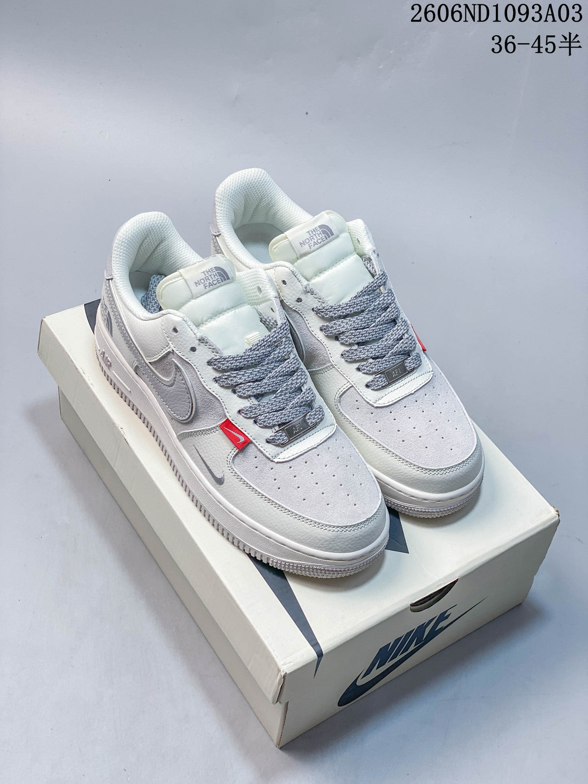 Pair of white and gray low-top sneakers with gray laces and red accent tabs on a shoebox