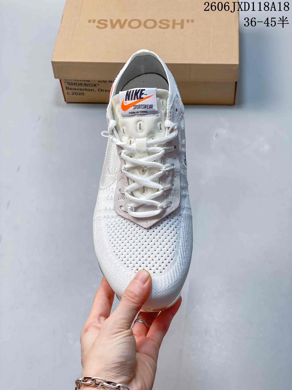 Front view of a white sneaker with white laces and orange tongue accent