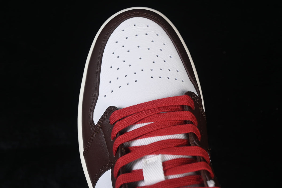 Top-down close-up of a perforated white toe box framed by dark brown overlays and red laces.