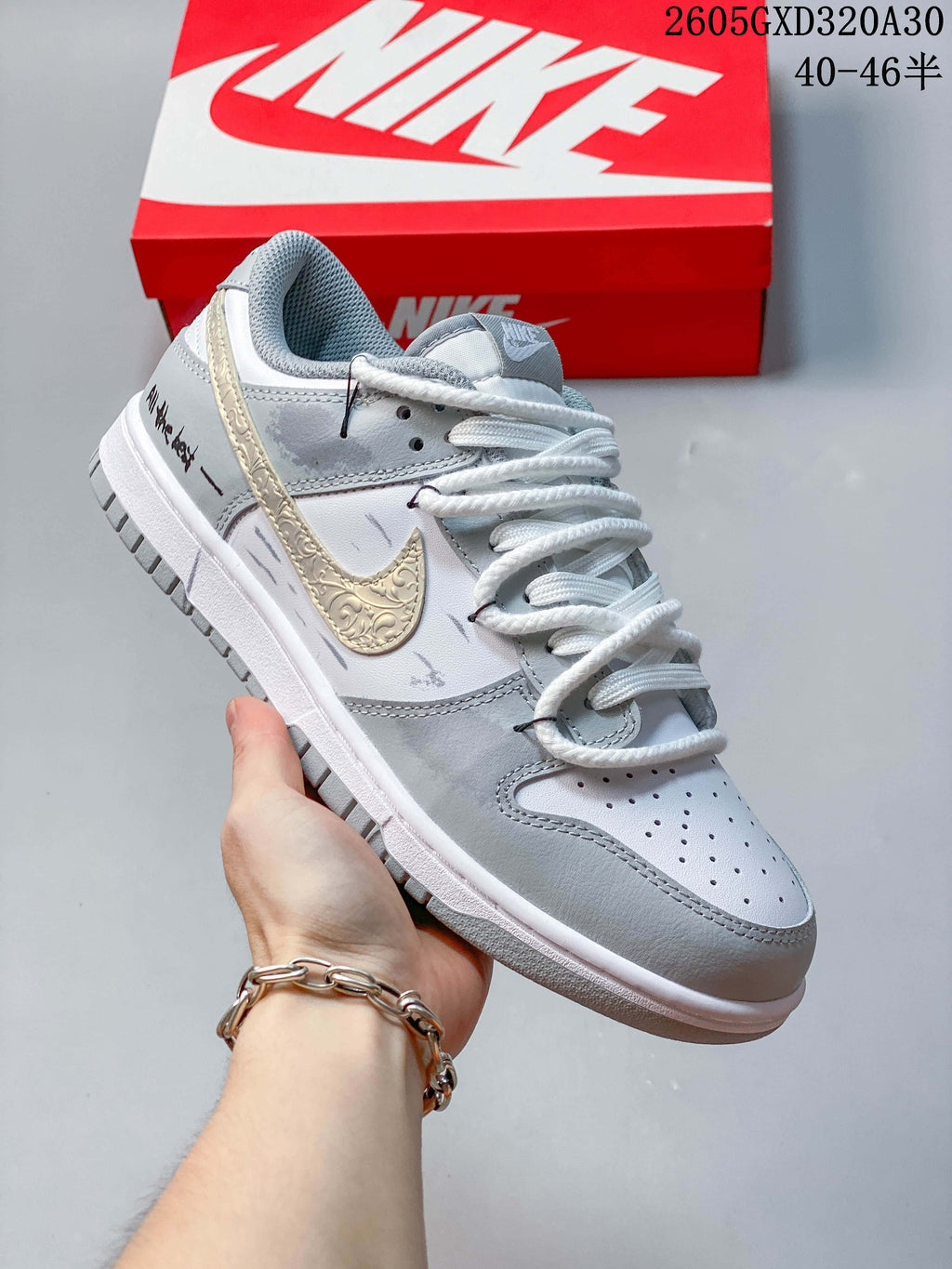 Side view of a white and gray low-top sneaker with a decorative gold-tone Swoosh and black heel lettering.