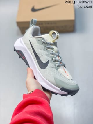 Angled view of a pale green and white Nike trail sneaker with a dark Swoosh, black toe bumper, and red outsole detail beside its shoe box.