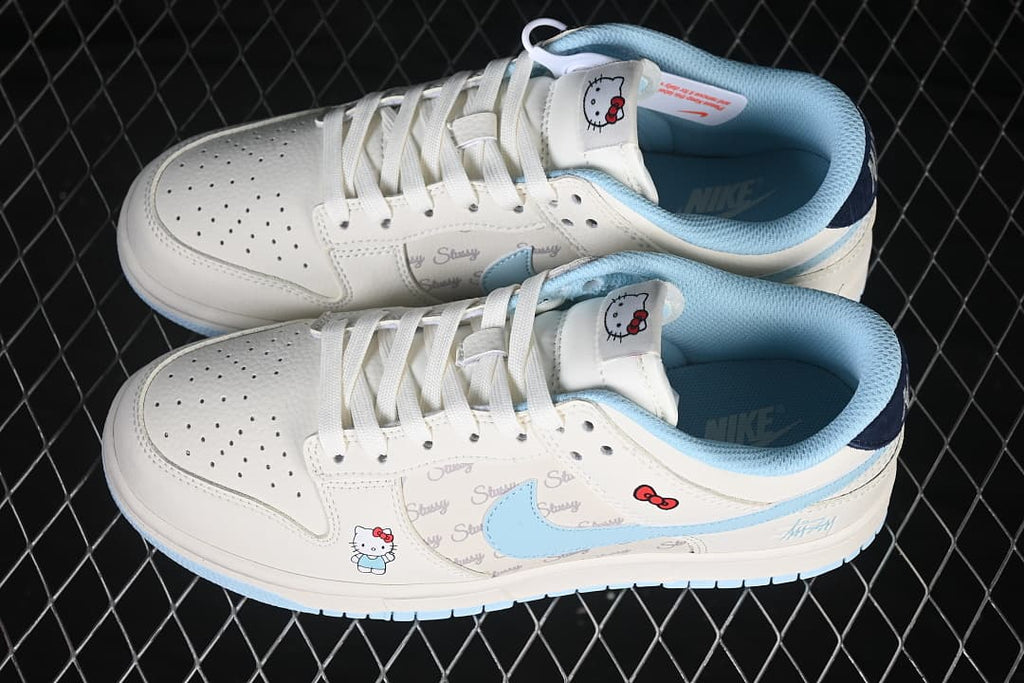 Pair of ivory and pale blue low-top sneakers with Hello Kitty graphics, script-print side panels, and blue Swooshes.
