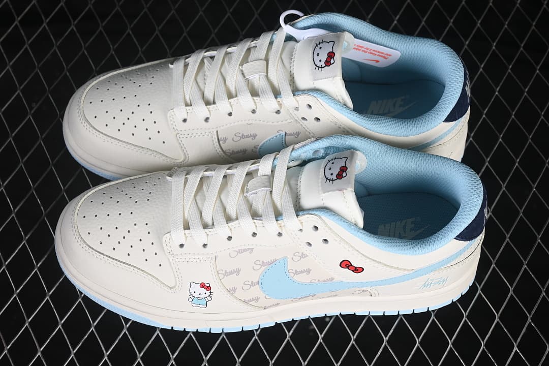 Pair of ivory and pale blue low-top sneakers with Hello Kitty graphics, script-print side panels, and blue Swooshes.