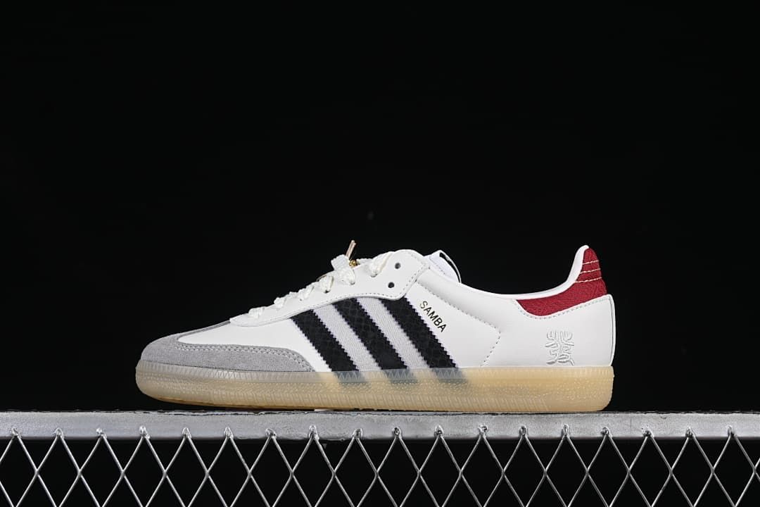 Side profile of white adidas Samba OG sneakers with black stripes, gray toe overlay, red heel detail, and gum outsole