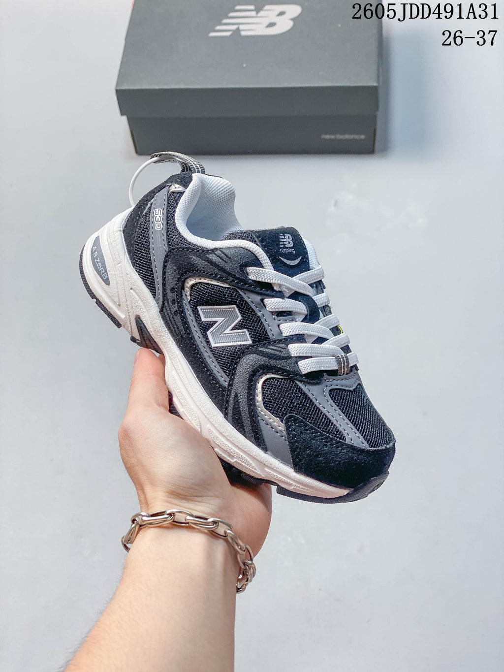 Black and gray kids' New Balance 530 lace-up sneaker shown in hand.