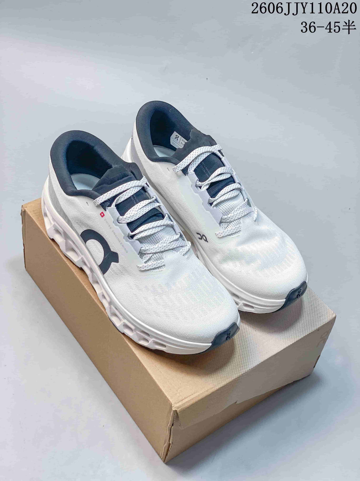 Pair of white On Cloudmonster 3 running shoes with dark navy details, shown on a box