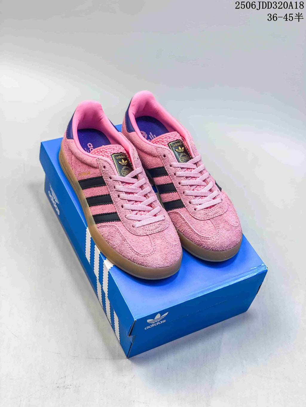 Pair of pink Adidas Gazelle sneakers with dark stripes and gum-colored soles, displayed on a blue shoe box.