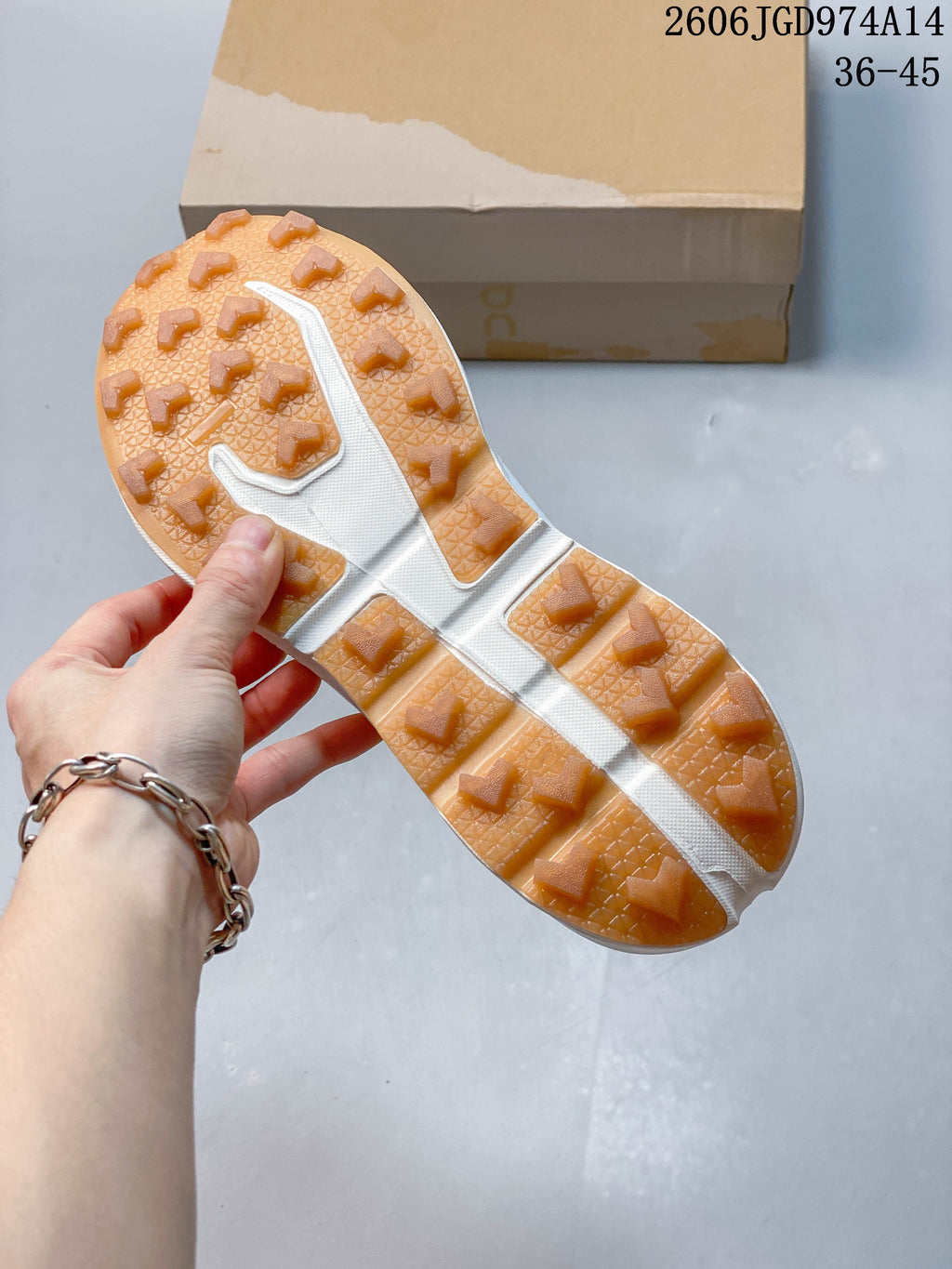 Close-up of the gum-colored lugged outsole on a white trail running shoe.