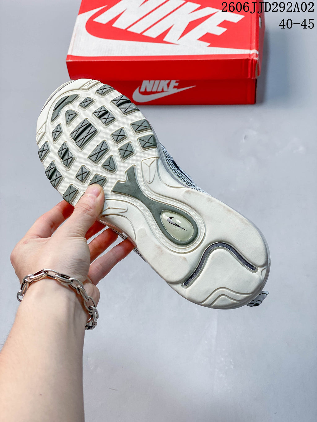 Outsole view of a Nike Air Max 97 sneaker with patterned tread and a red shoe box behind it