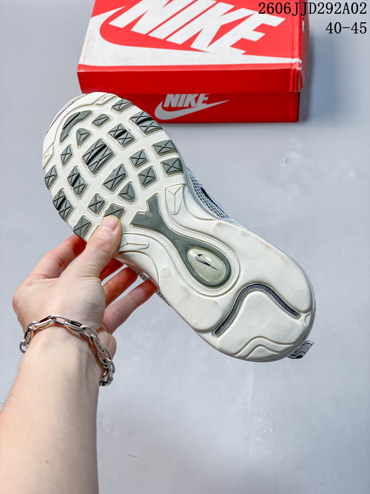 Outsole view of a Nike Air Max 97 sneaker with patterned tread and a red shoe box behind it