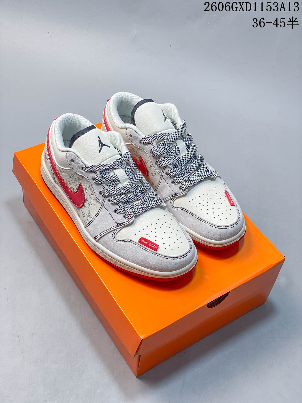 Pair of light-colored low-top sneakers with red accents and patterned laces on an orange box