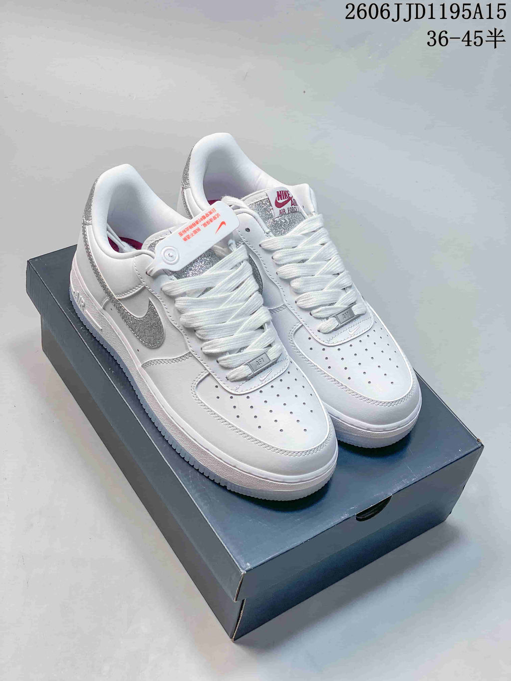 White low-top sneakers with silver reflective-look Swoosh accents, shown on a shoe box.