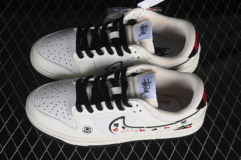 Pair of white low-top sneakers with black laces, perforated toe panels, and decorative graphics, viewed from above.