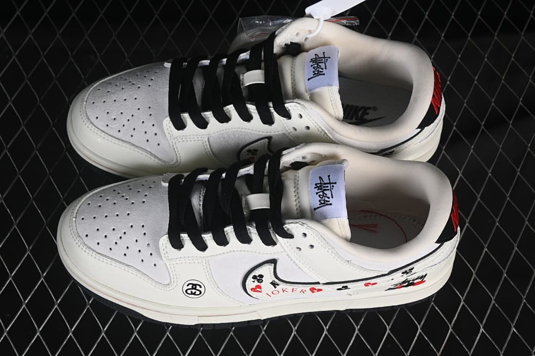 Pair of white low-top sneakers with black laces, perforated toe panels, and decorative graphics, viewed from above.
