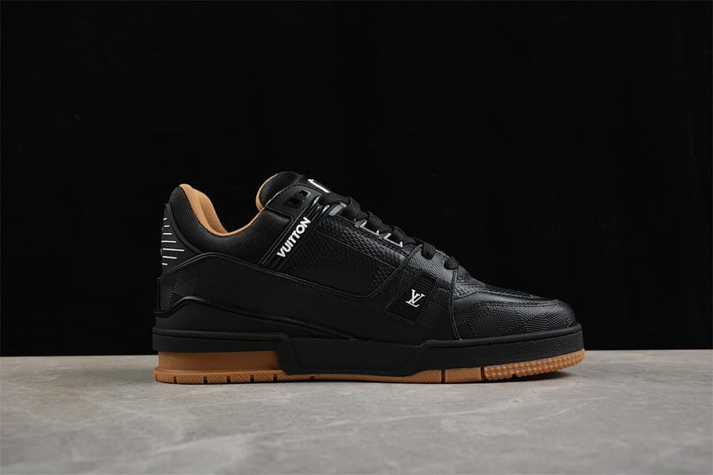 Side view of a black low-top sneaker with logo details and a tan-colored outsole