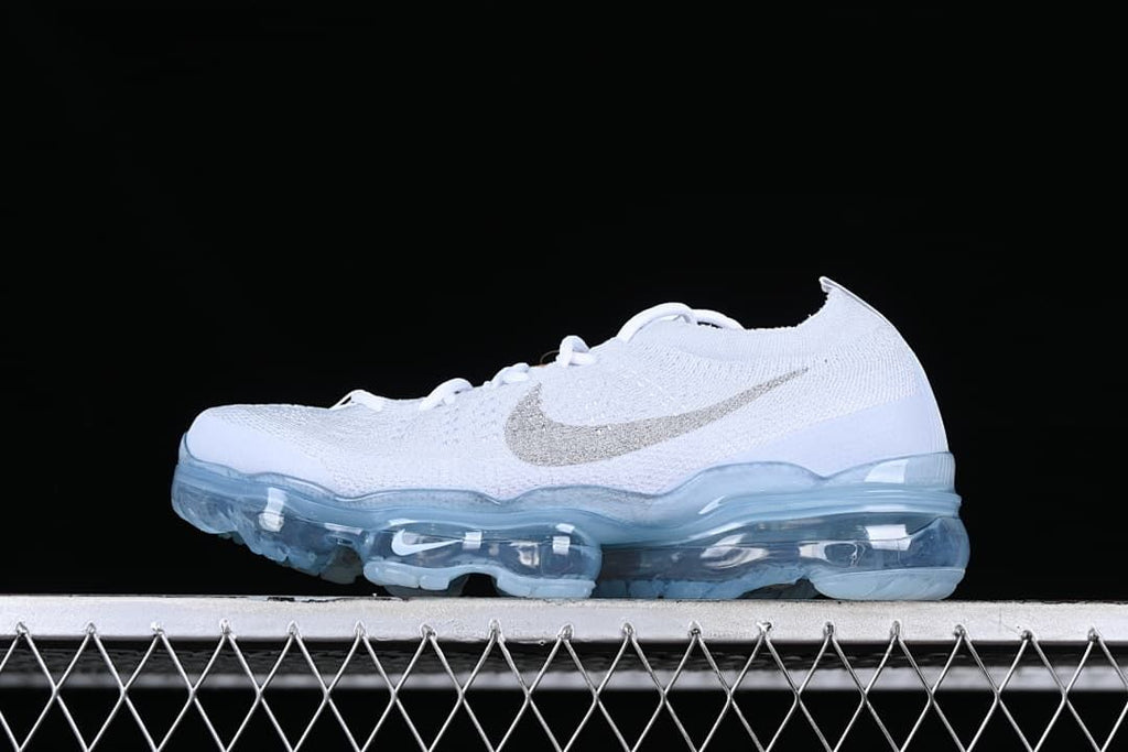 White Nike Air VaporMax 2023 Flyknit sneaker with metallic-look Swoosh and translucent blue sole, side view