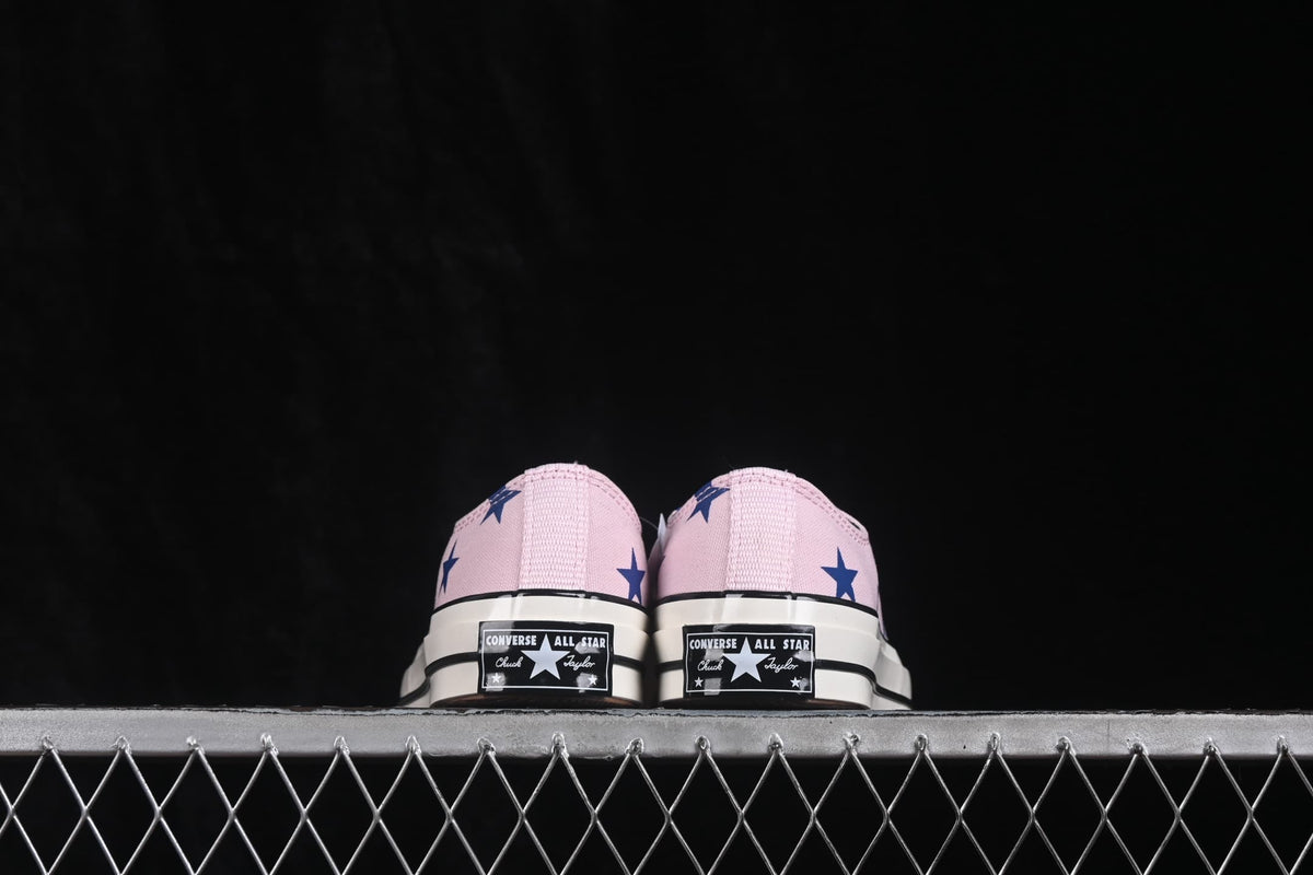 Rear view of pink low-top sneakers with blue star graphics and Converse All Star heel labels.