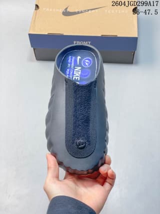 Top view of a dark gray-black Nike Mind 001 slide held above its shoebox, showing the closed toe and upper panel.
