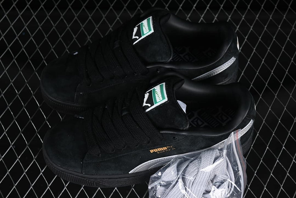 Pair of black and silver Puma Suede XL sneakers with an additional pair of light-colored laces.
