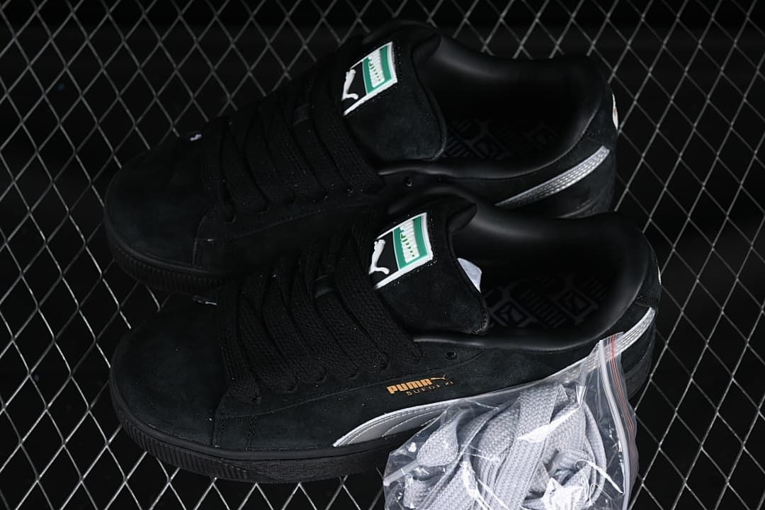 Pair of black and silver Puma Suede XL sneakers with an additional pair of light-colored laces.