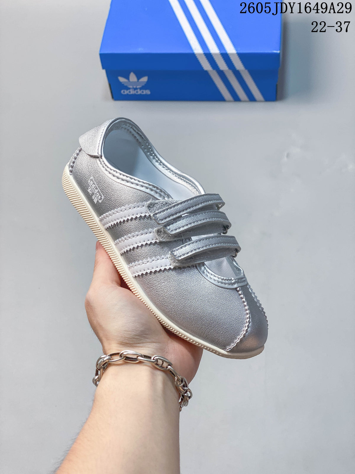 Angled side view of the silver sneaker with three stripes and hook-and-loop straps