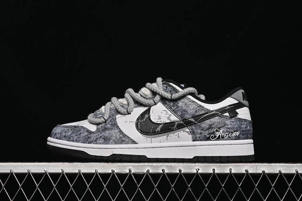 Side view of a grey, black, and white Nike SB Dunk Low sneaker with thick grey laces and “Angeles” heel embroidery