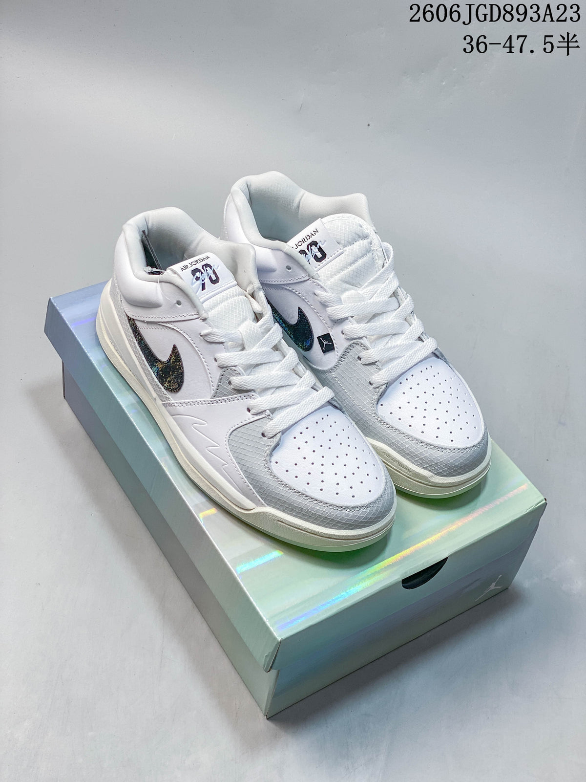 Pair of white and grey Jordan Stadium 90 sneakers with iridescent Swooshes, shown on a box.