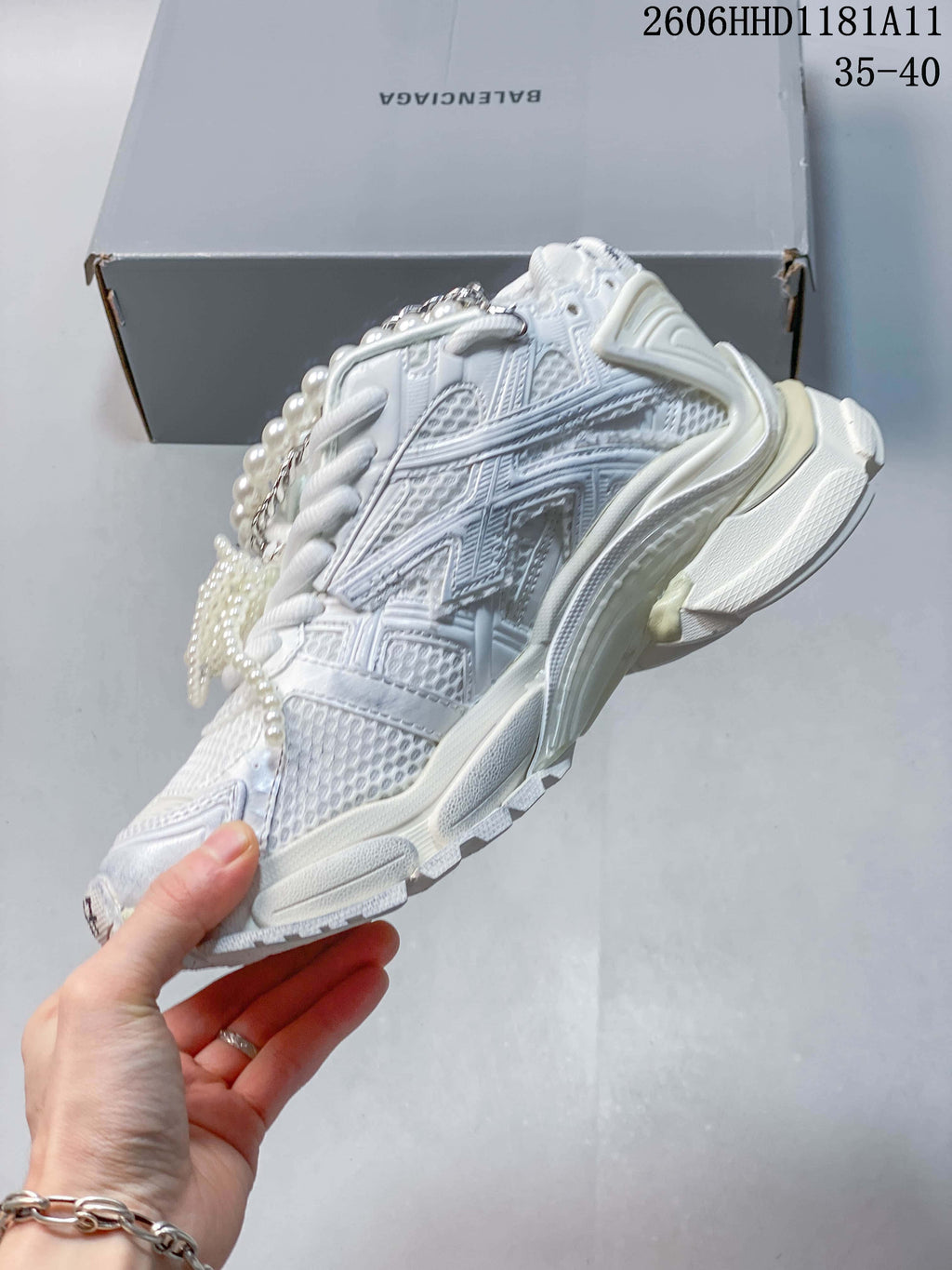Side view of the white sneaker with a layered upper, chunky sole, and lace embellishments.