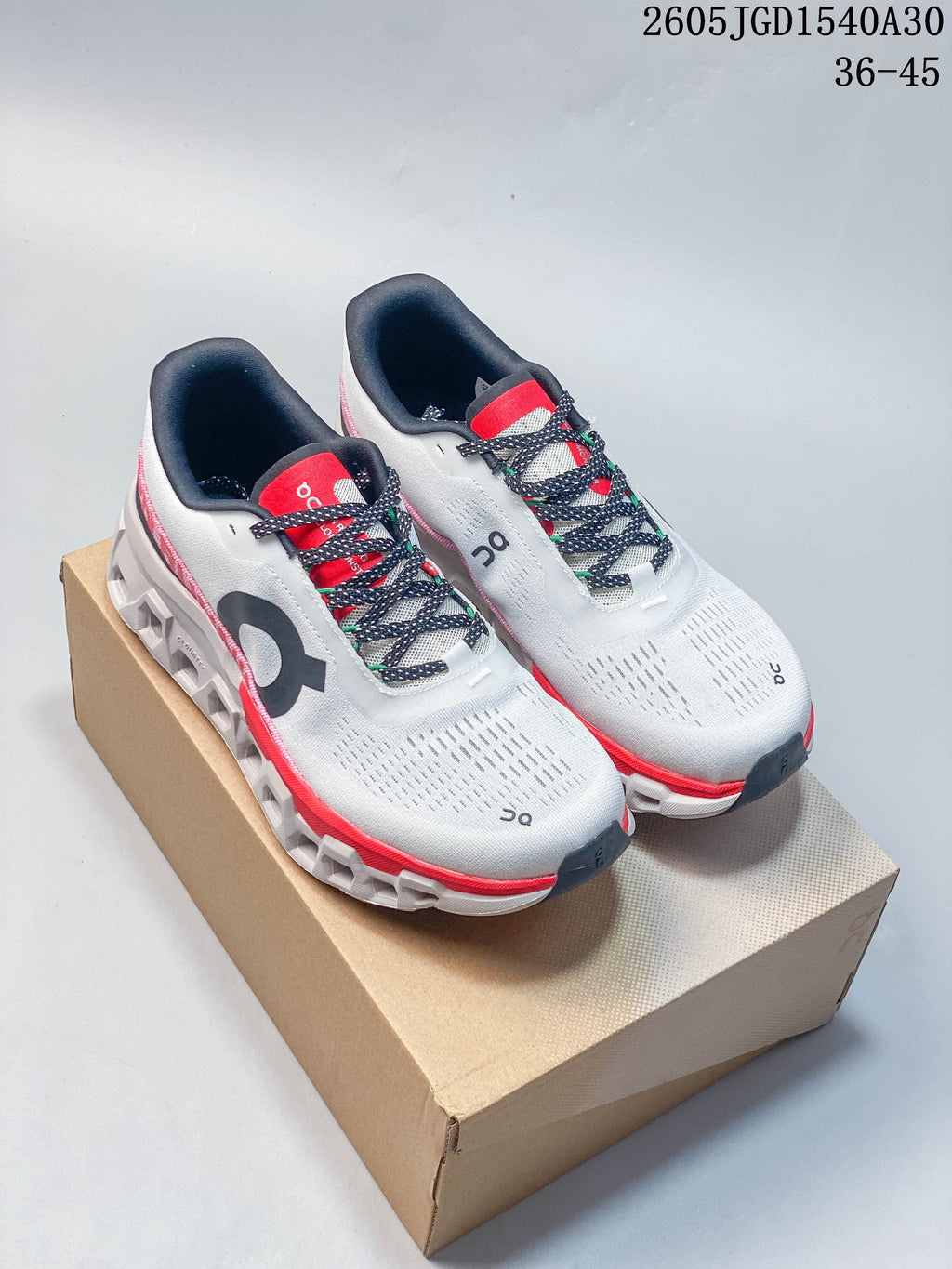 Pair of white On Cloudmonster 2 shoes with coral and navy accents on a shoebox