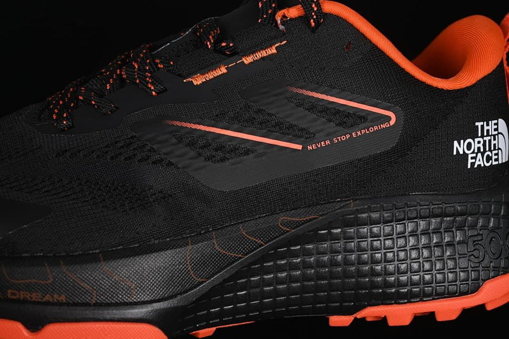 Close-up of the black and orange lace-up upper and side branding.