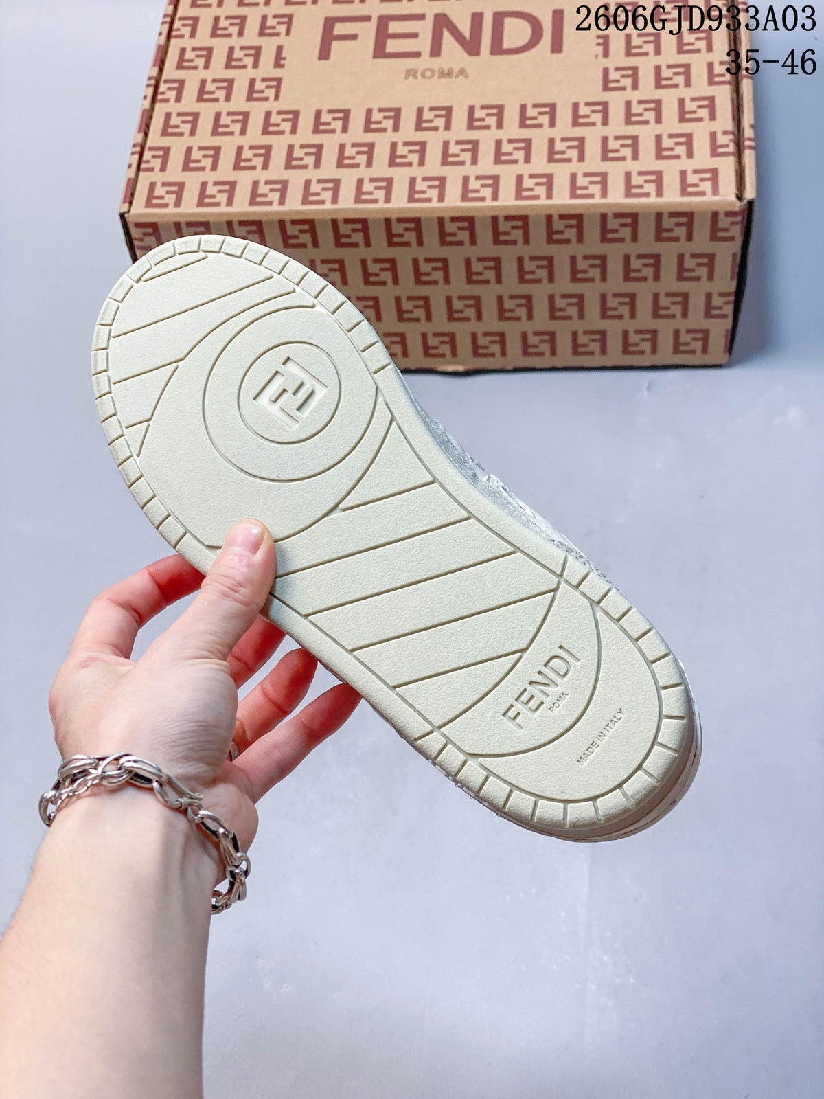 Underside of a white sneaker with a patterned shoe box in the background; image overlay shows 2606GJD933A03 and sizes 35–46.