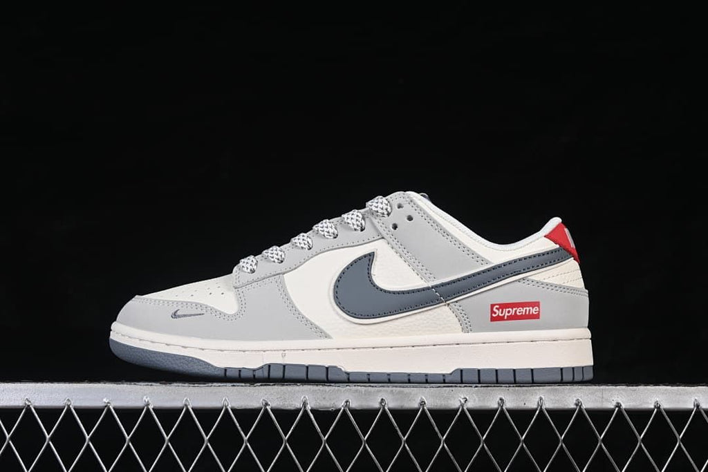 Side view of a grey and off-white Nike SB Dunk Low sneaker with a dark grey Swoosh and red accents.