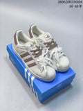 Pair of off-white Adidas Superstar sneakers with brown and gray accents, shown on a blue box.