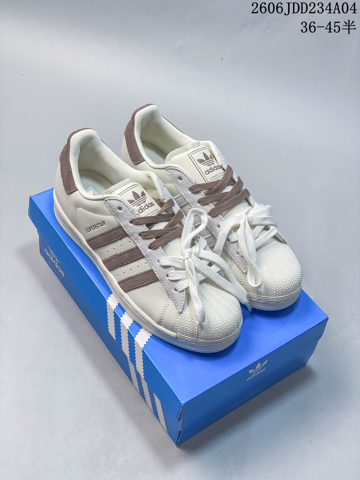 Pair of off-white Adidas Superstar sneakers with brown and gray accents, shown on a blue box.
