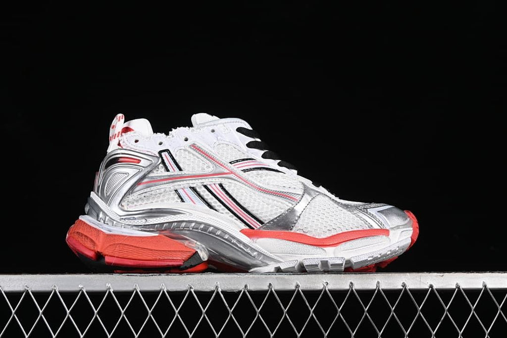 Side profile of the white sneaker with silver-toned overlays and red outsole accents.