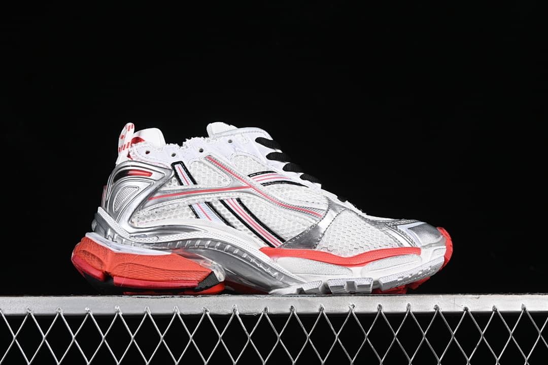 Side profile of the white sneaker with silver-toned overlays and red outsole accents.