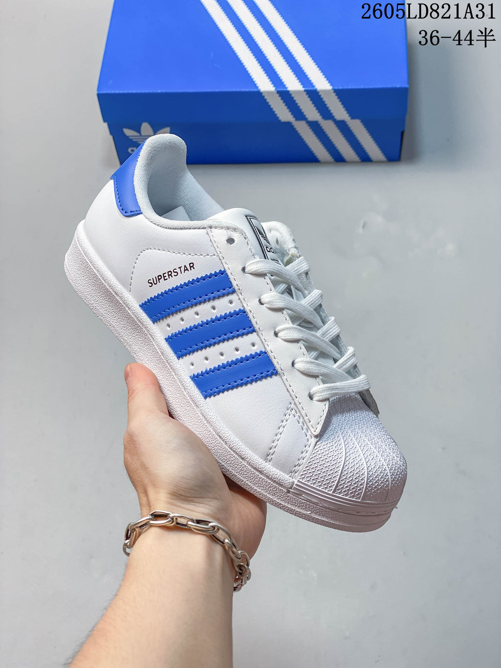 White adidas Superstar sneaker with blue stripes and a textured shell toe.