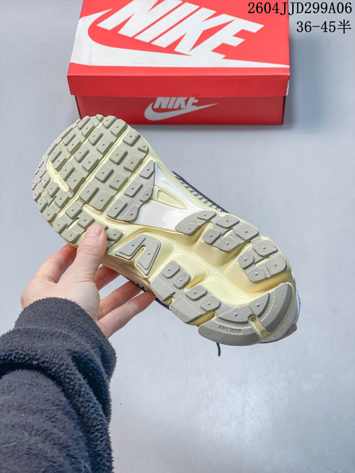 Underside view of a Nike Zoom Vomero 5 sneaker showing its patterned outsole; a red shoe box is in the background.