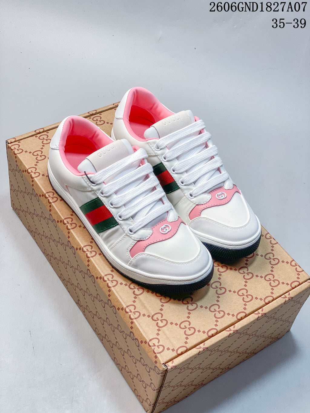 Pair of white and pink low-top sneakers with green-and-red side stripes, shown on a patterned shoe box.